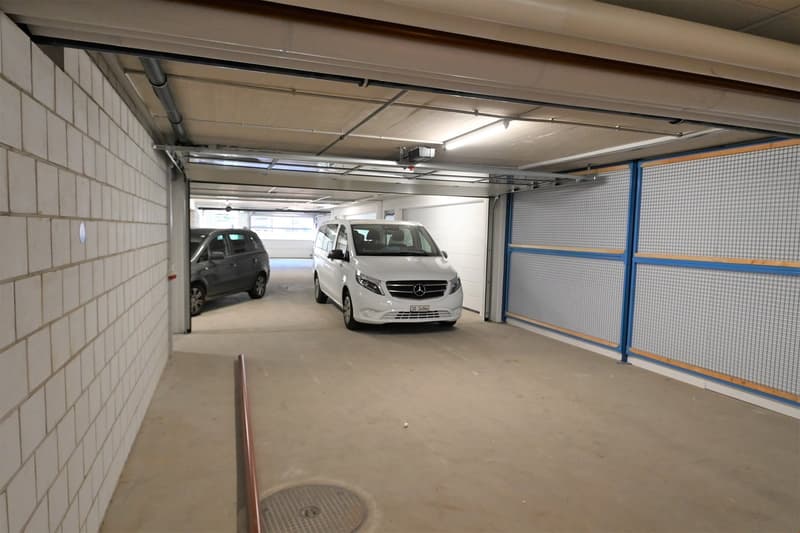 Two cars parked, concrete walls, overhead lighting, ventilation ducts