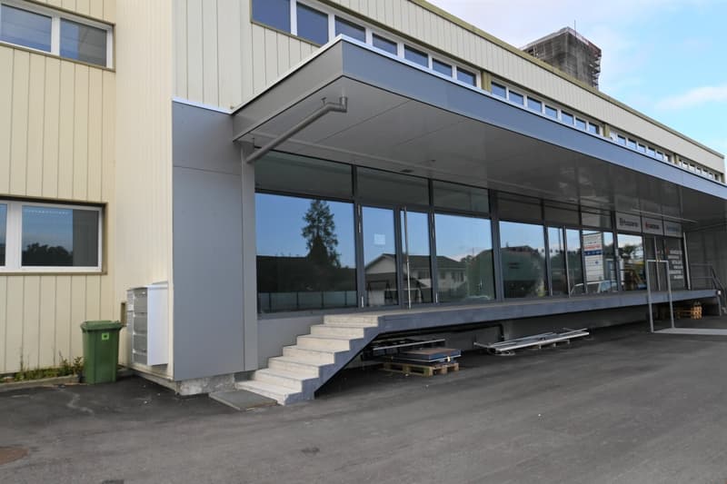 modern building with glass facade, concrete steps, metal awning, trash bin, and a parking lot