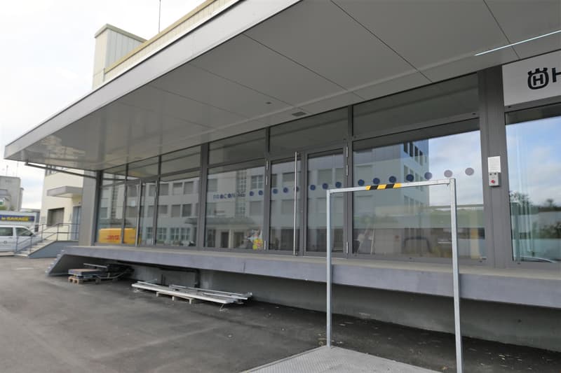 modern building with glass walls, entrance with automatic sliding doors, large parking area, stairs leading to the entrance