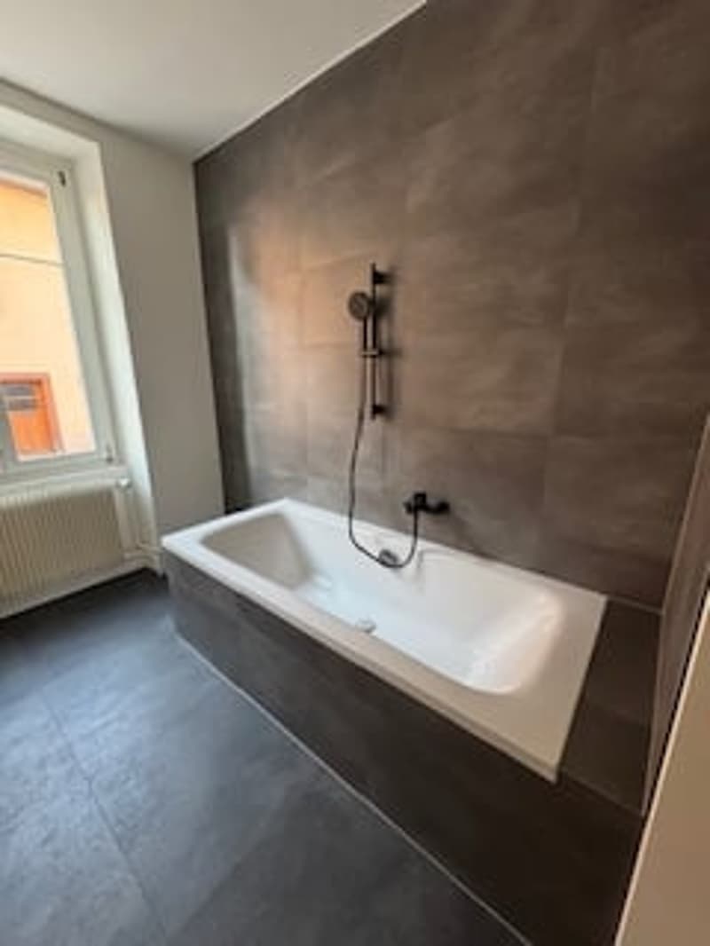 Bathroom with bathtub, shower head, radiator, window