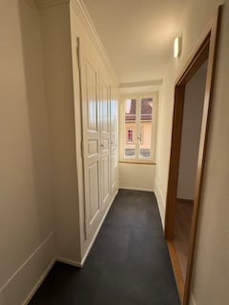 Empty hallway with white walls, black floor, white doors, window with white frame