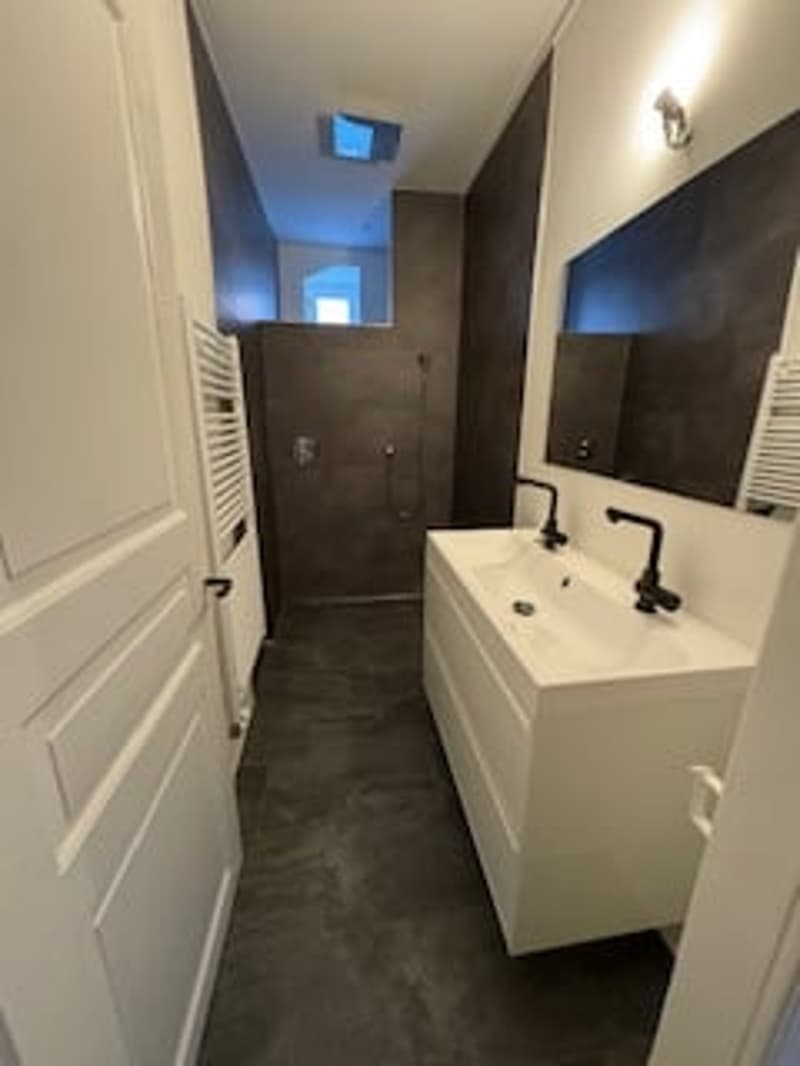 Bathroom with a white sink, black faucets, a large mirror, and a shower area with a glass door.
