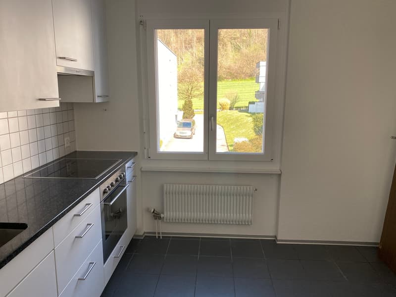 modern kitchen with white cabinets, black countertops, gas stove, oven, sink, window with view of a car and grassy field