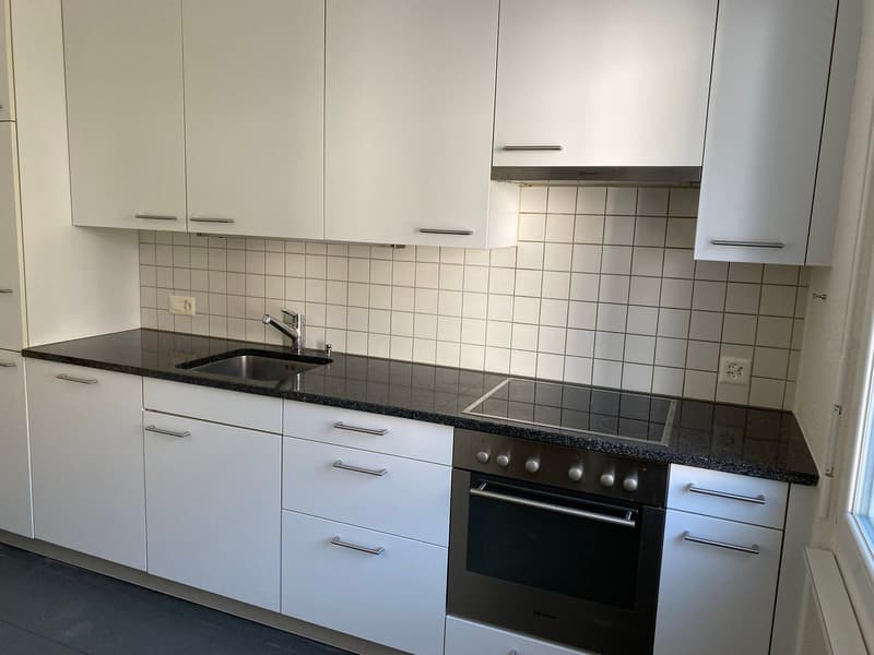 modern kitchen with white cabinets, black countertops, stainless steel sink, gas stove, oven, tiled walls, electrical outlets, and a window