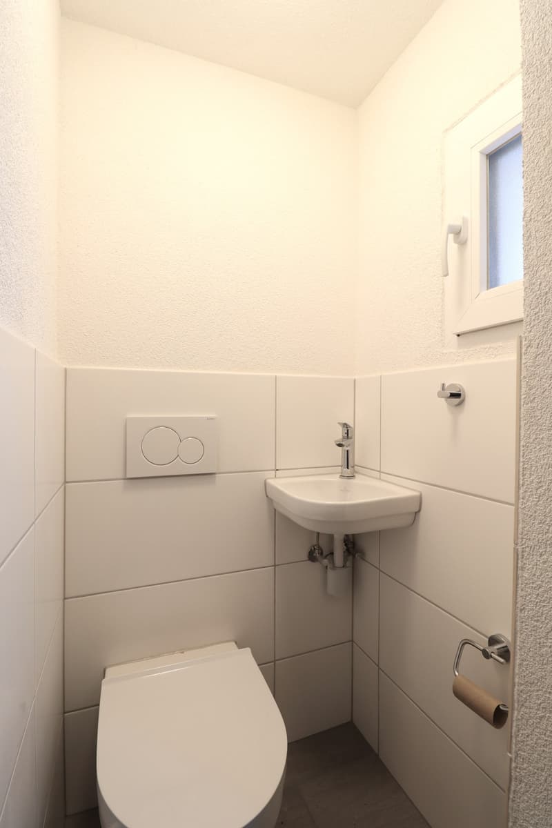 Small bathroom with white tiles, a toilet, and a sink with a faucet. The room has a simple, minimalist design.