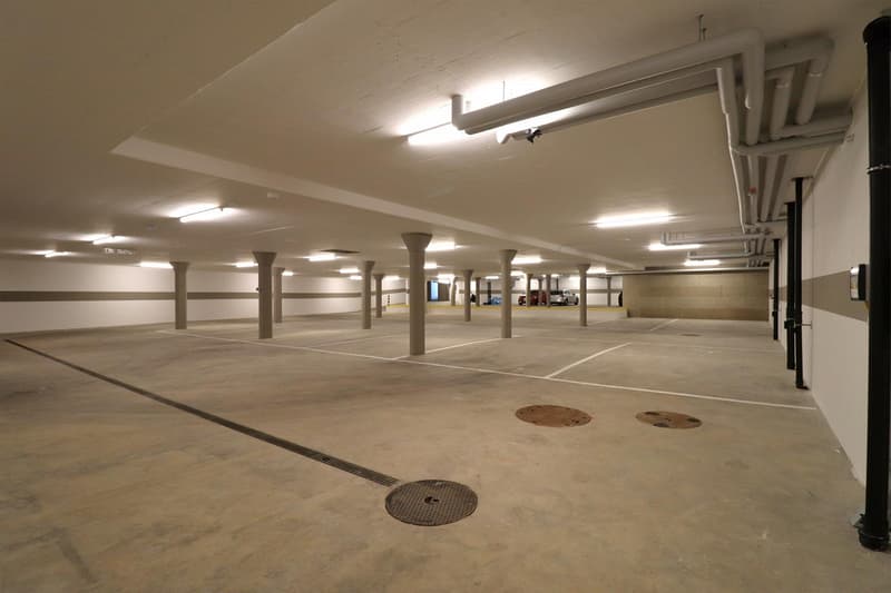 empty underground parking lot with several concrete pillars and lights mounted on the ceiling