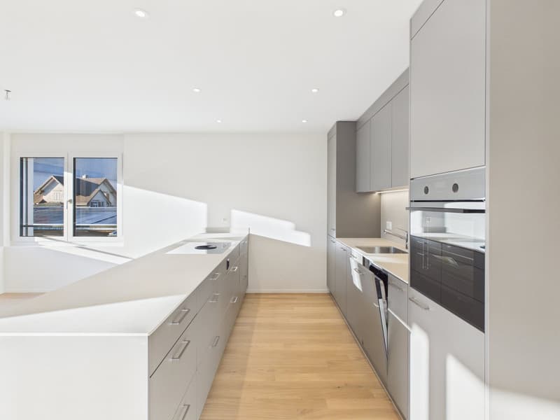 Modern kitchen with white countertops, gray cabinets, large windows, and integrated appliances.