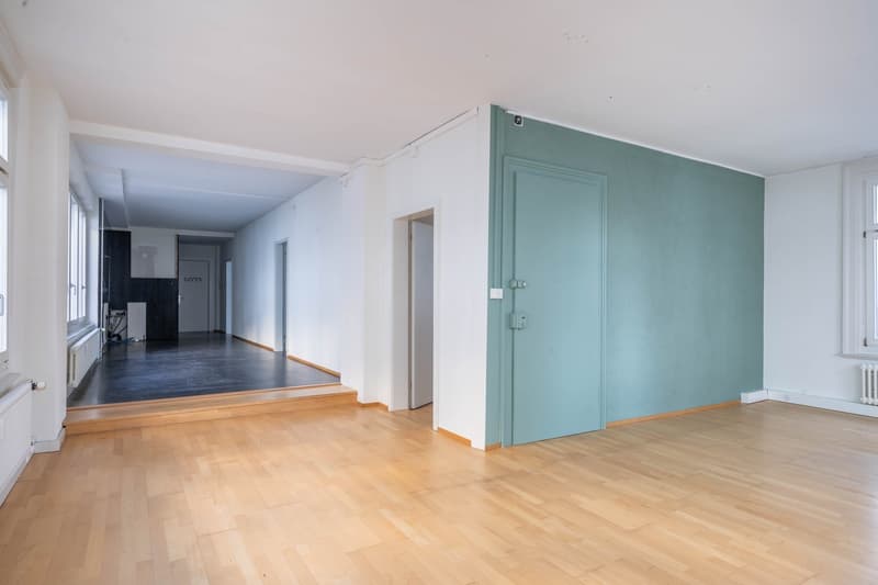 empty room with wooden floors, white and green walls, radiators, and multiple windows