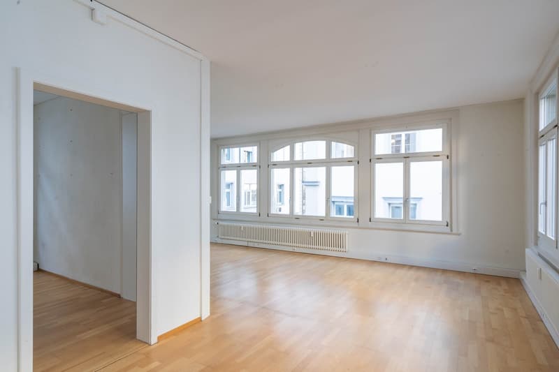 Wooden floors, white walls, multiple large windows, and no furniture