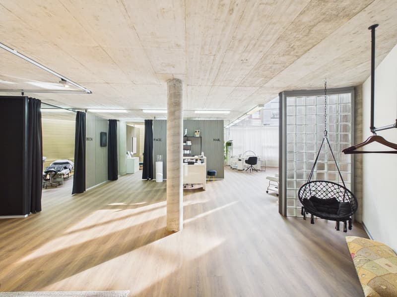 Spacious interior with wooden floors, exposed concrete ceiling, medical equipment, swing chair, and various decorative items.