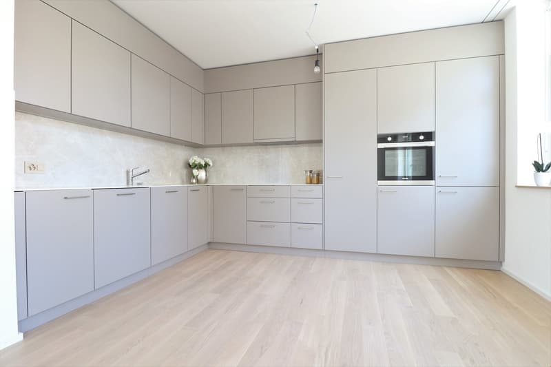 modern kitchen with white marble countertops, gray cabinets, stainless steel sink, faucet, built-in oven, dishwasher, and a potted plant on the window sill