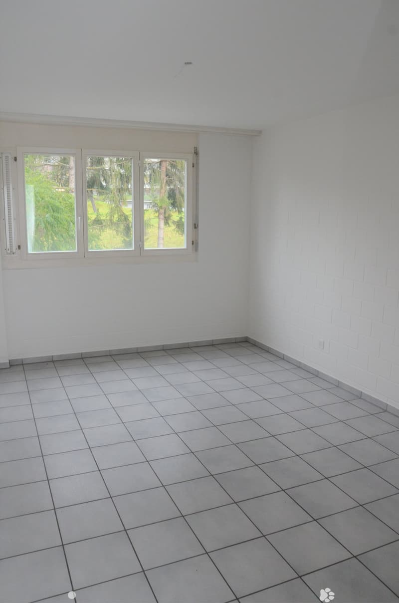 empty room, white walls, gray tile flooring, three windows, electrical outlet on right wall