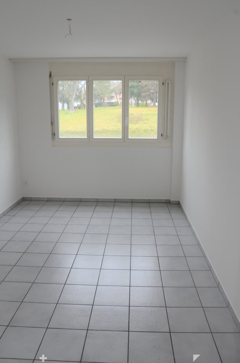 an empty room with white tiled floor, a window with white frame and view of a grassy field