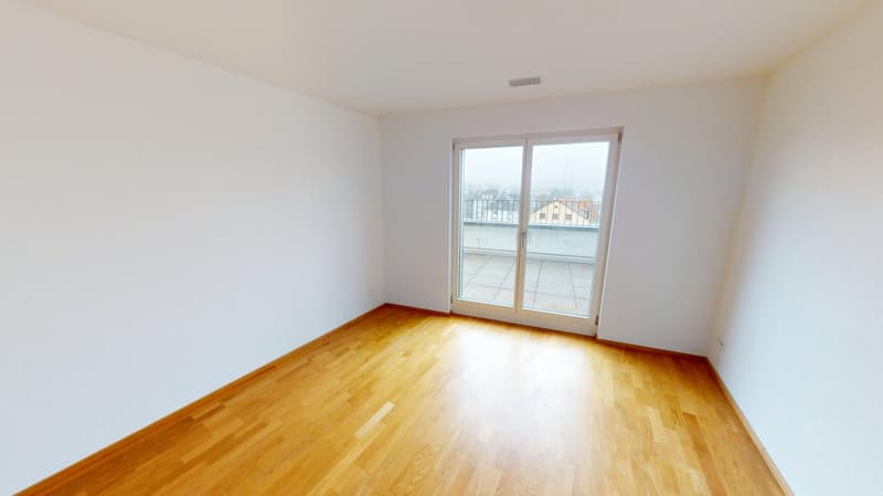 Empty room with wooden floor, sliding glass doors leading to balcony, white walls, power outlets.