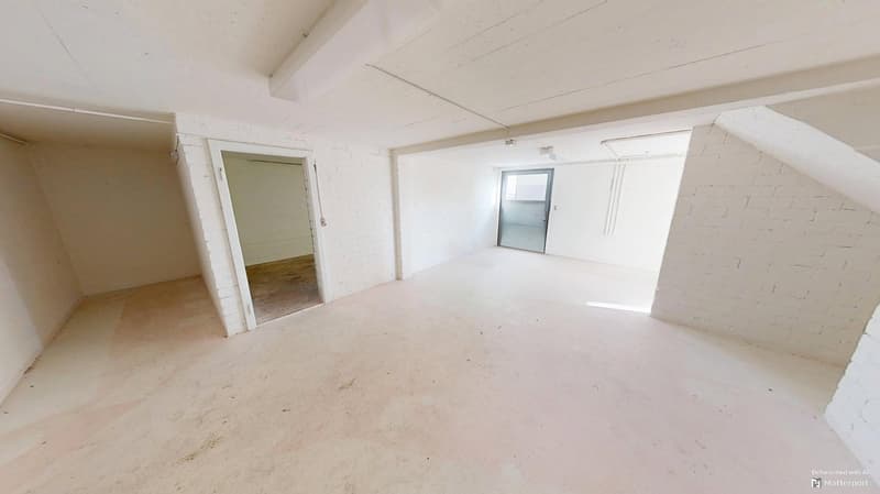 White brick walls, concrete floor, two doors, one leading to a small room