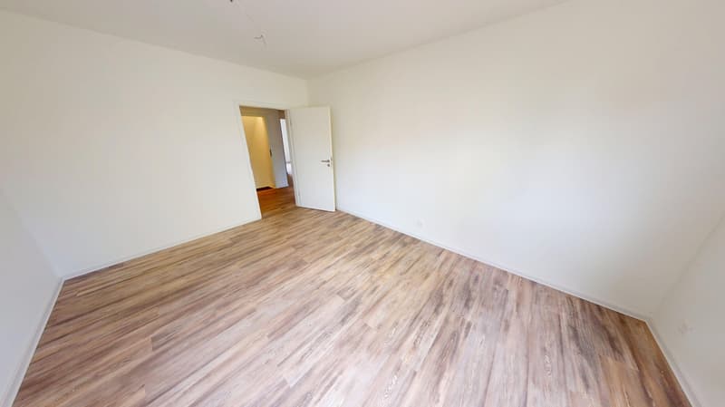 empty room with wooden floors, white walls, two doors, one leads to another room