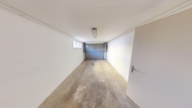 white walls, grey concrete floor, closed door, grey garage door, small window