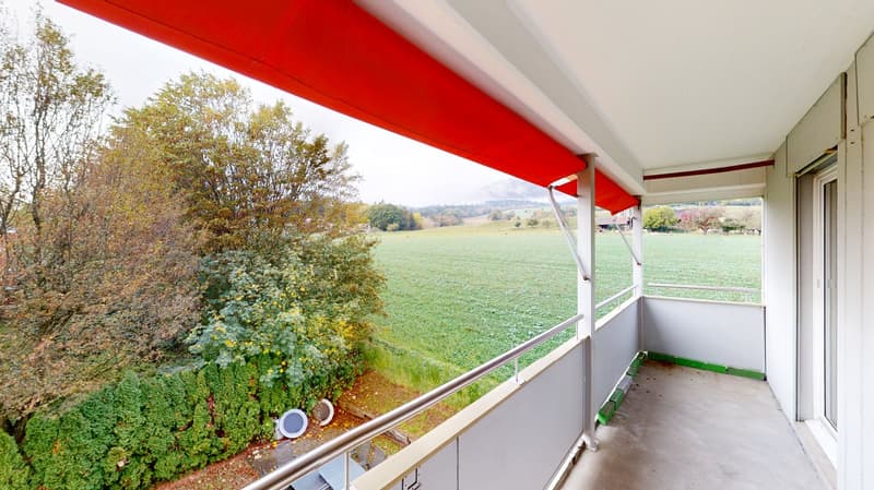 Balcony with red awning, metal railing, green field view