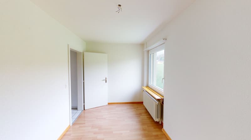 Empty room with white walls, wooden floor, white door, window with white frame, radiator