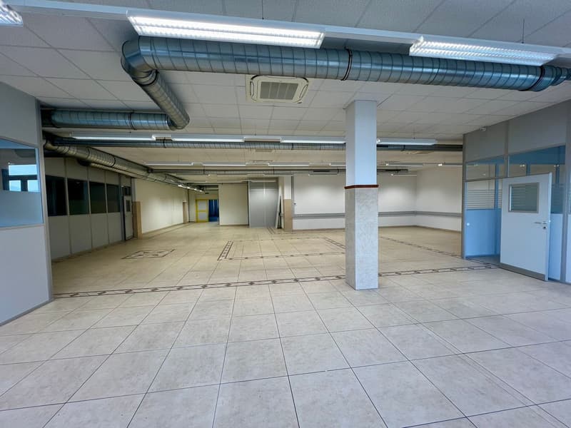 Large open commercial space with tiled flooring, exposed ceiling ductwork, and a column in the center. The space appears to be unoccupied and ready for potential tenants or businesses to move in.