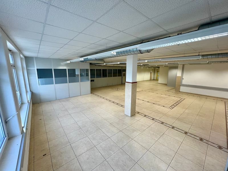 Large open office space with a tiled floor, suspended ceiling tiles, and glass partitions. The space appears to be empty and ready for use.