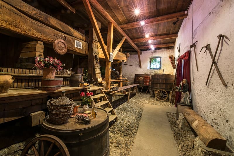 Wooden beams, rustic decor, barrels, shelves, stairs, fireplace, wheels, picture frames, statues, stone flooring