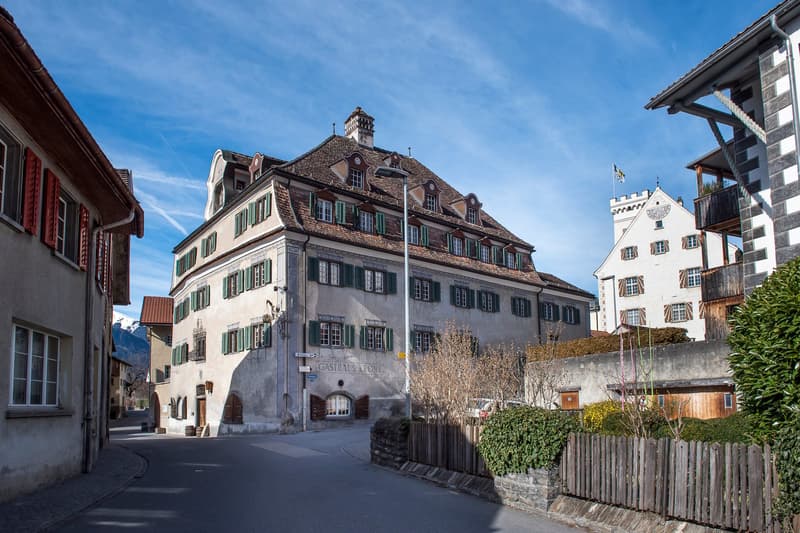 large building with multiple windows and balconies, concrete walls and metal roof, with mountain in the distance