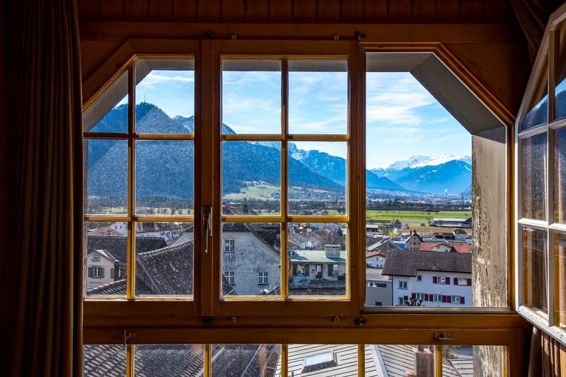 Mountains, city, and sky through a wooden framed window.