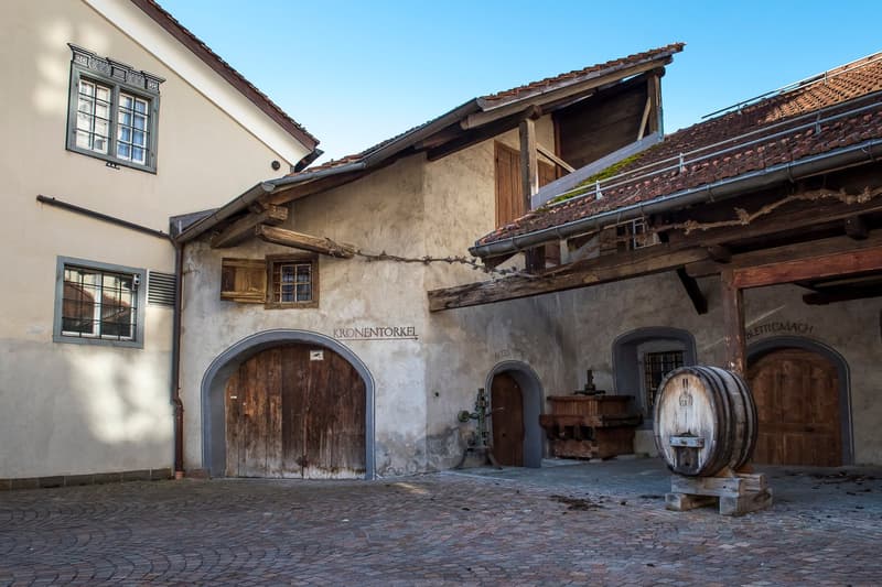 Old wooden building with brick walls, arched doorways, cobblestone courtyard, large barrel, signboard