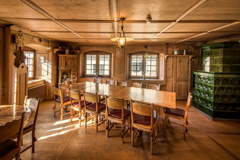 large dining table with chairs, wooden cabinet, hanging lamps, radiator, windows