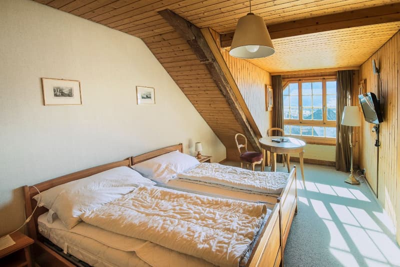 Room with two beds, white bedding, wooden wall, two chairs, table, TV
