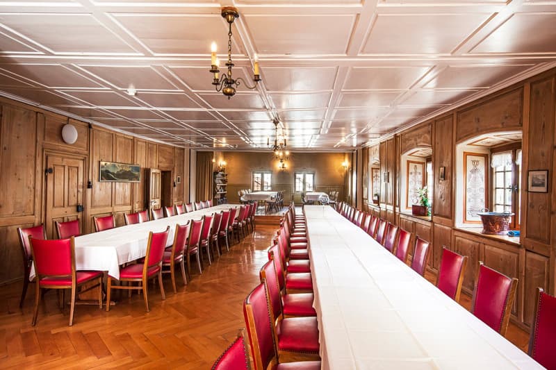 Dining room: wooden wall, chandelier, long tables, wooden chairs, window, plant in window