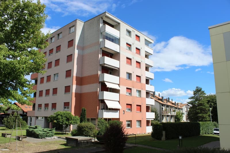 Multi-story building, multiple balconies, red shutters, beige and pink exterior, trees and bushes in front