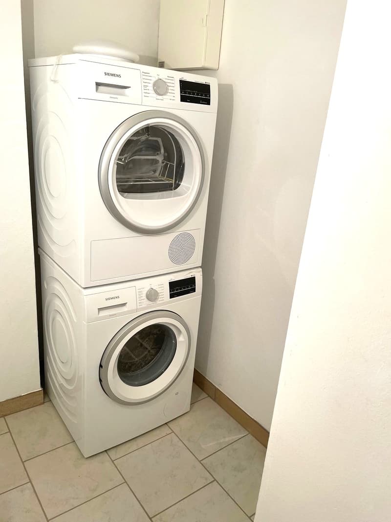 Stacked washing machine and dryer, Siemens brand, white tiled floor, white walls