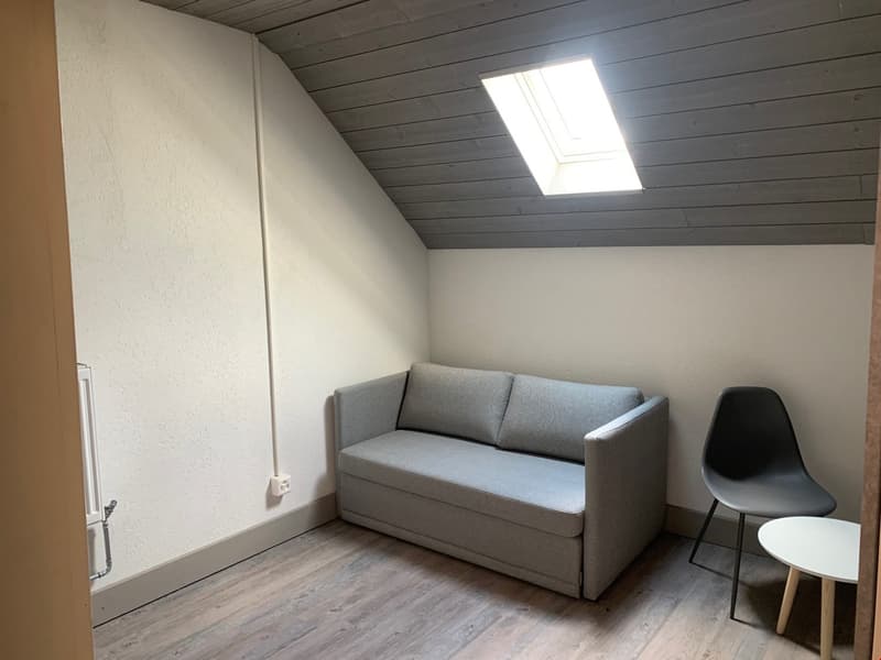 Attic bedroom with slanted ceiling, gray sofa, black chair, and small side table