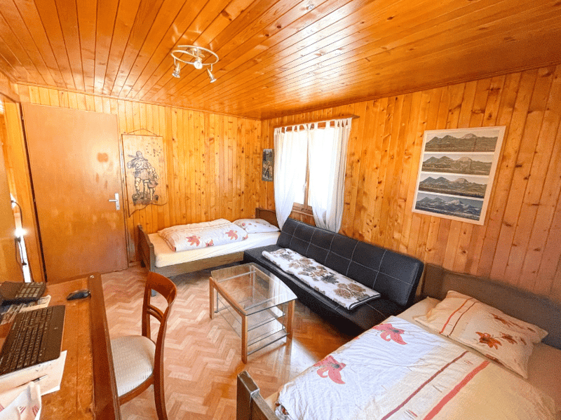 room with wooden walls, two beds, a couch, a desk, a chair, a glass table, a lamp, a picture on the wall