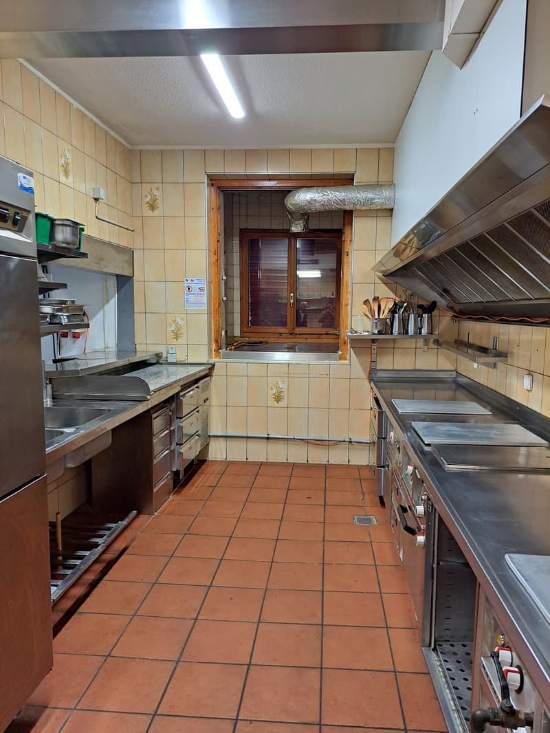 Commercial kitchen with tile flooring, wooden cabinets, stainless steel appliances including a dishwasher, and a window