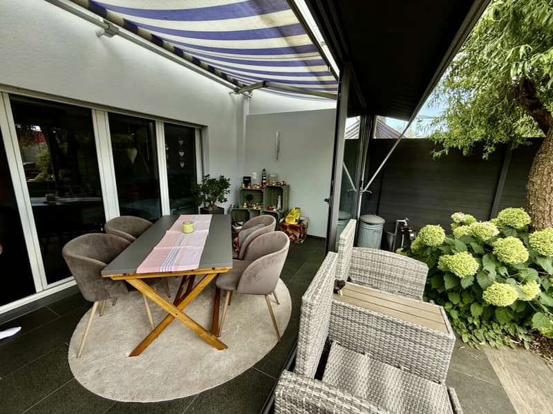 Der gedeckte Sitzplatz und im Hintergrund der Wintergarten.