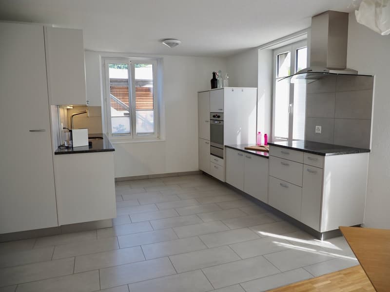 Modern kitchen with tiled floor, white cabinets, gray countertops, overhead lighting, built-in oven, microwave, and refrigerator.