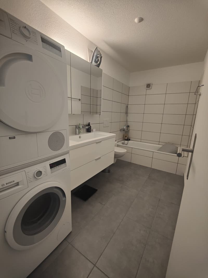 modern bathroom with white tiles, bathtub, toilet, sink, washing machine, and dryer