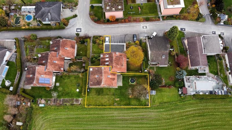 Terraced houses, red roofs, garages, and a large green yard. Cars parked.