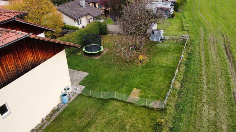 2 story house, brown roof, beige exterior, small garden, trampoline, shed