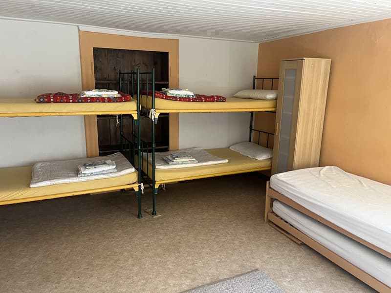 Three bunk beds with mattresses, a wooden wardrobe with glass doors, and a small rug