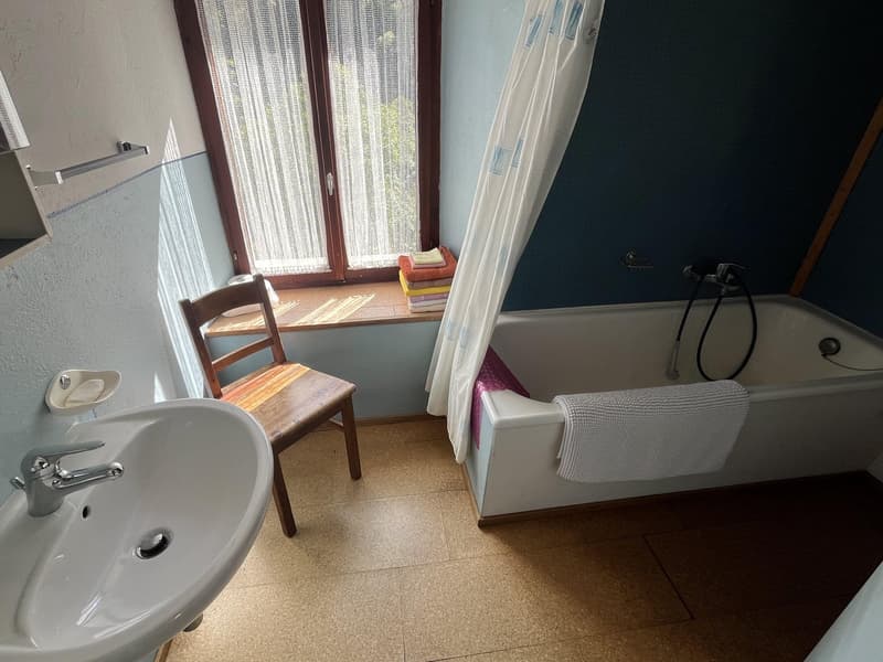 Bathroom with a bathtub, sink, wooden chair, and towels on the window sill.