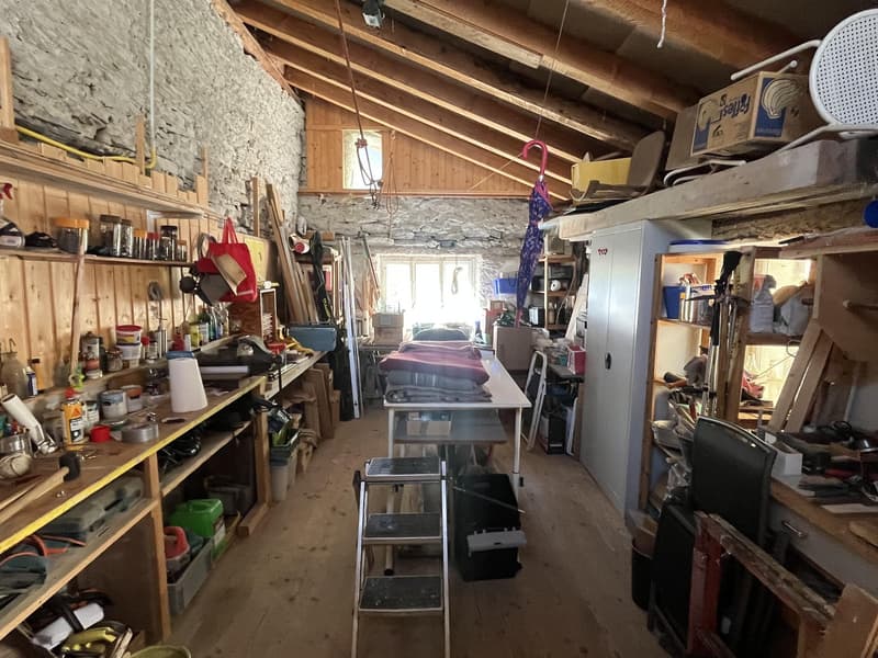 Stone walls, wooden shelves, ladder, various items, desk, black trash bin, white tablecloth, windows