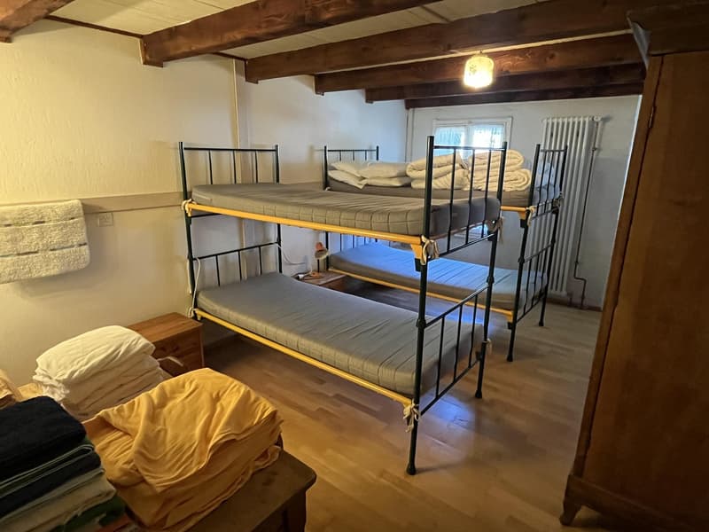 A room with wooden floors, exposed wooden beams, bunk beds, a nightstand, a radiator, and a towel hanging on the wall.