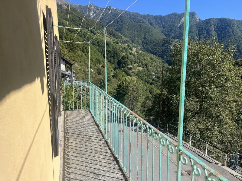 Balcony, green railings, concrete floor, yellow wall, scenic mountain view, lush greenery