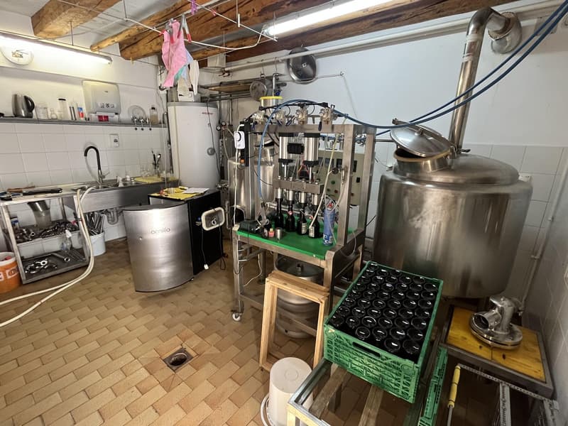 tiled floor, industrial setting, large stainless steel tanks, brewing equipment, wooden counter, storage crates, metal pipes, light fixtures