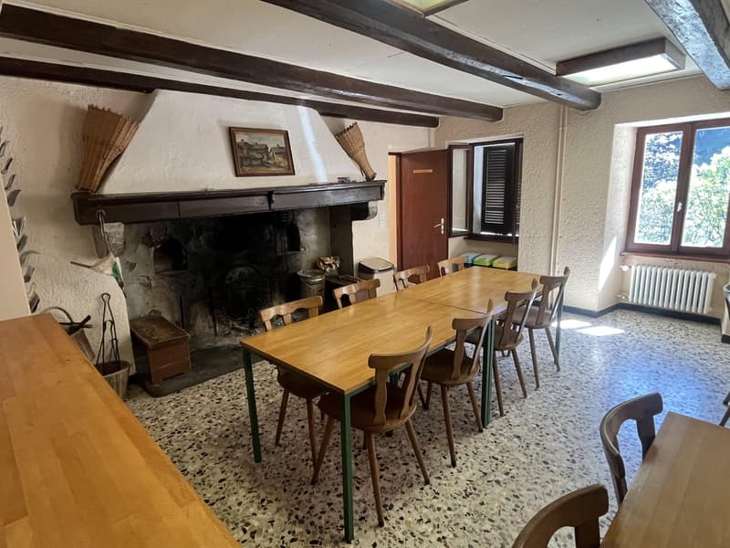 Dining area with a large dining table, chairs, wooden floor, fireplace, and windows