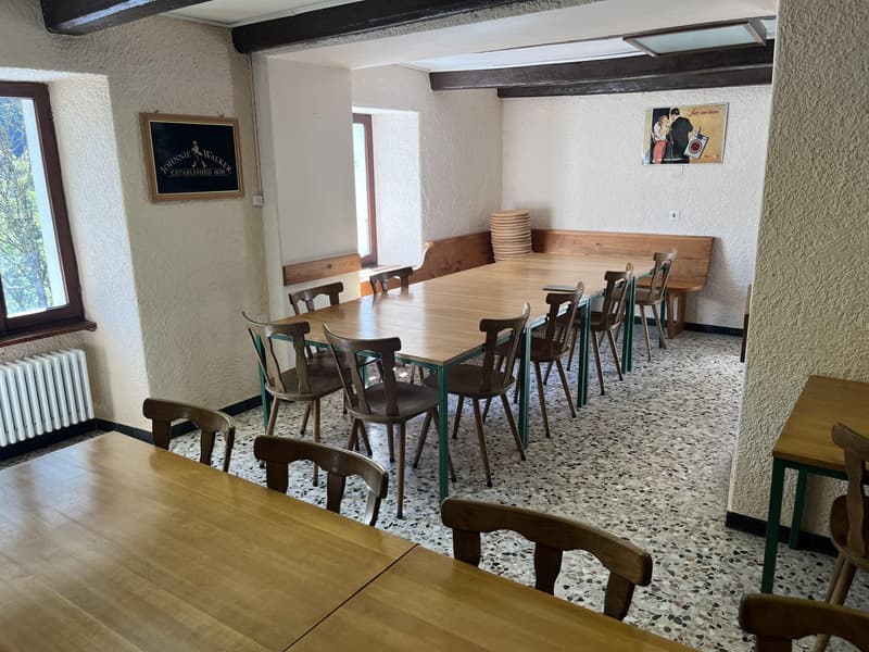 Long wooden table with chairs, wooden benches against the wall, two small windows, wooden framed black board on the wall